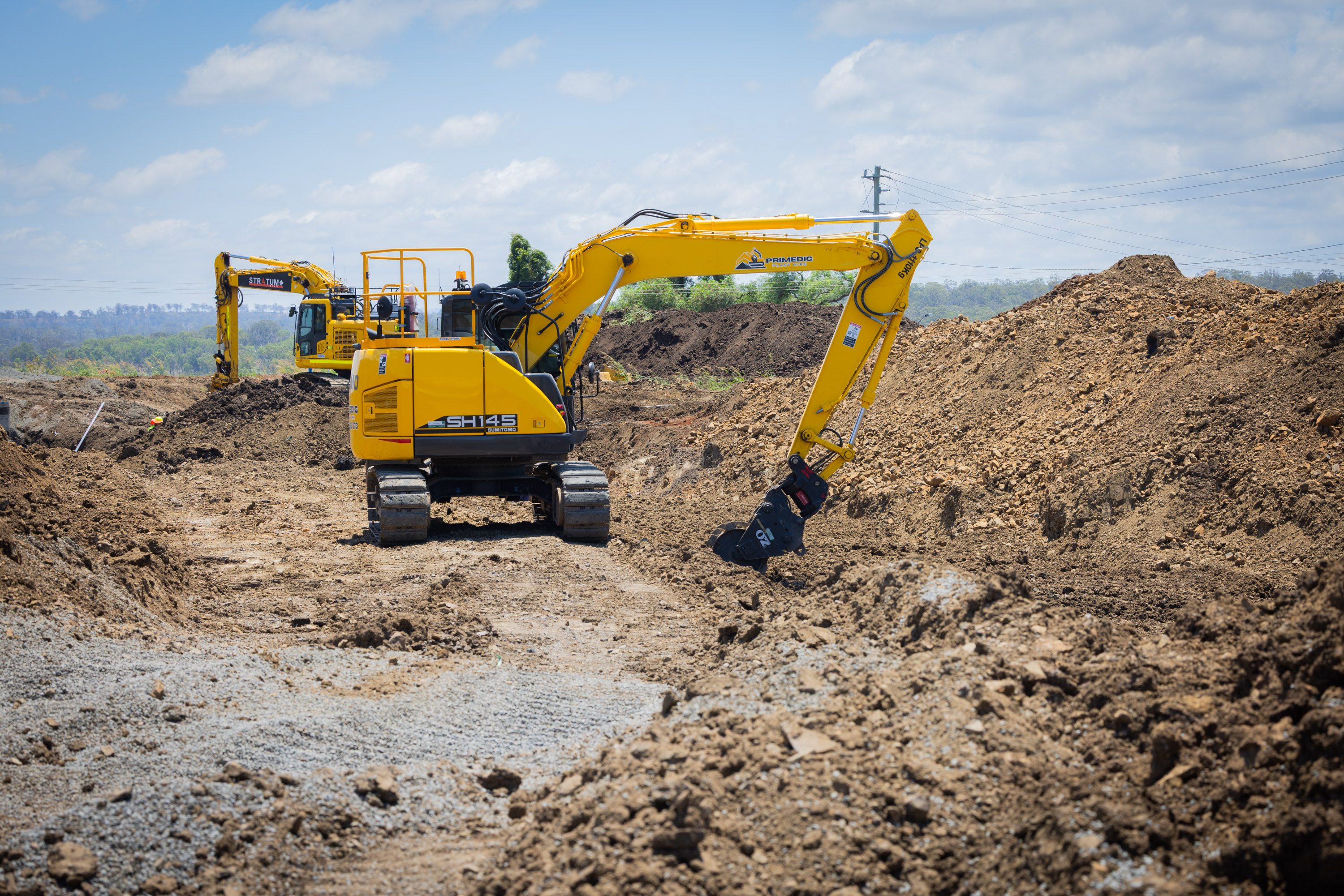 Sumitomo excavator with a tilt hitch working across a gravel earthworks site